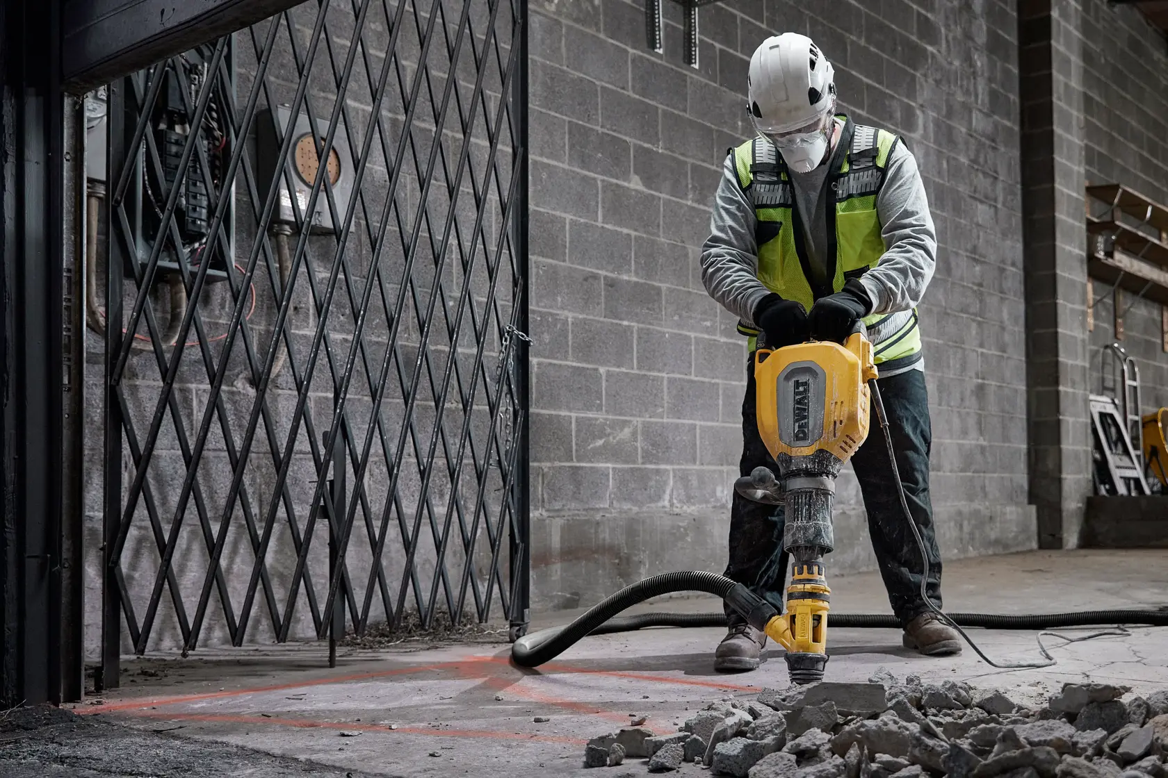Trabajador rompe suelo de hormigón con martillo DEWALT D25911K, escombros sobre el suelo.