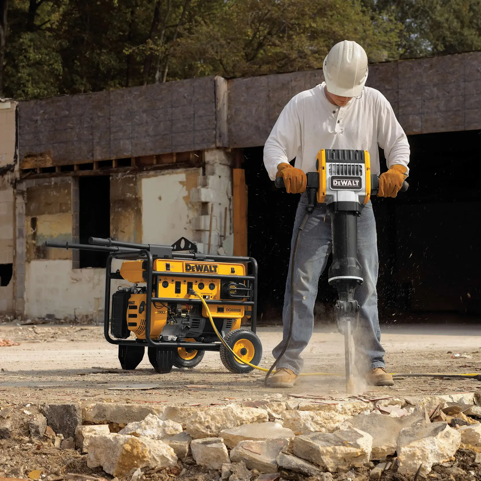 Un trabajador de construcción con casco, guantes y botas de trabajo opera un martillo neumático DEWALT rompiendo concreto, con un generador DEWALT en el fondo en un sitio de demolición al aire libre.