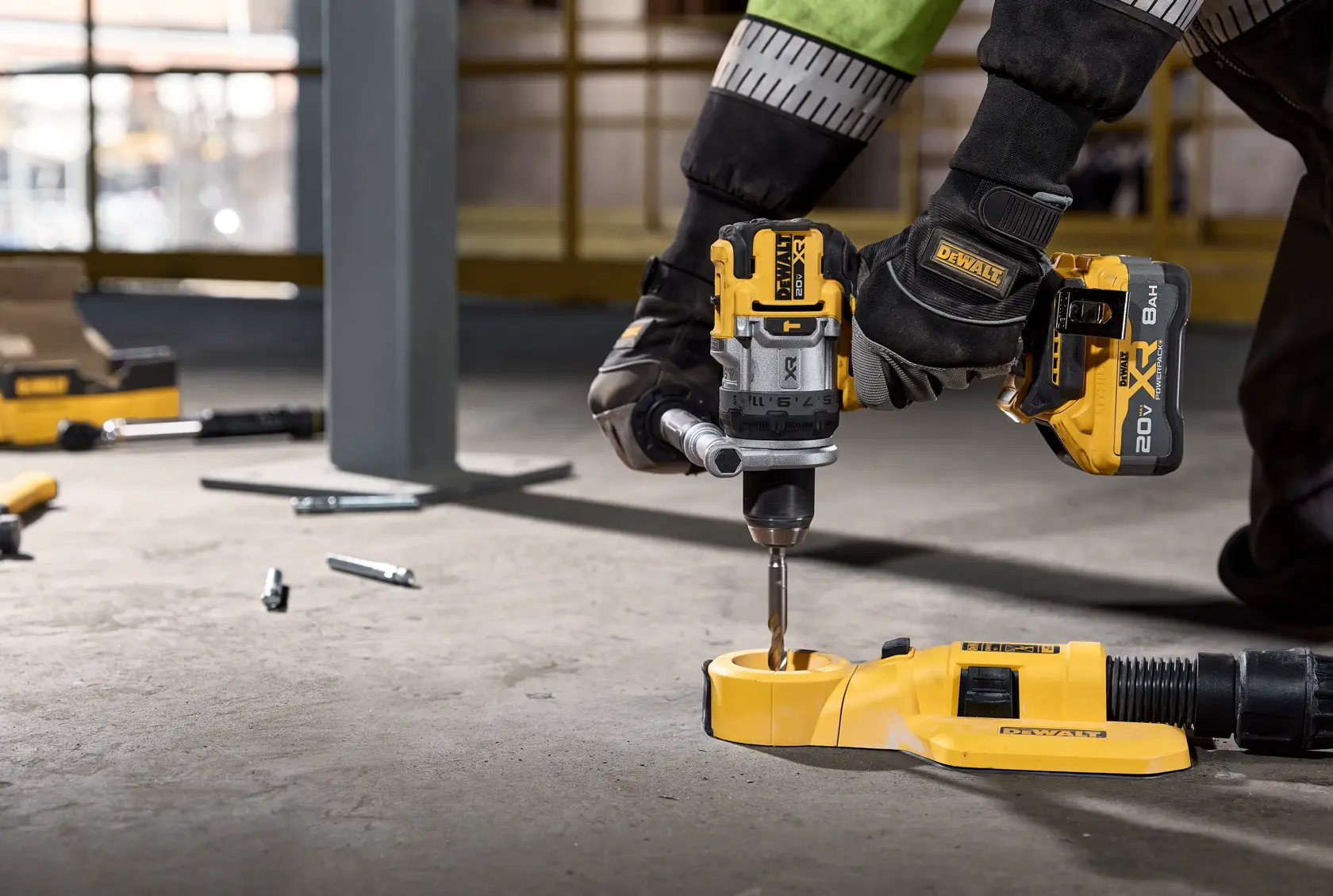 Mano con guante usando taladro DEWALT inalámbrico en piso de obra, con herramientas y tornillos cerca.