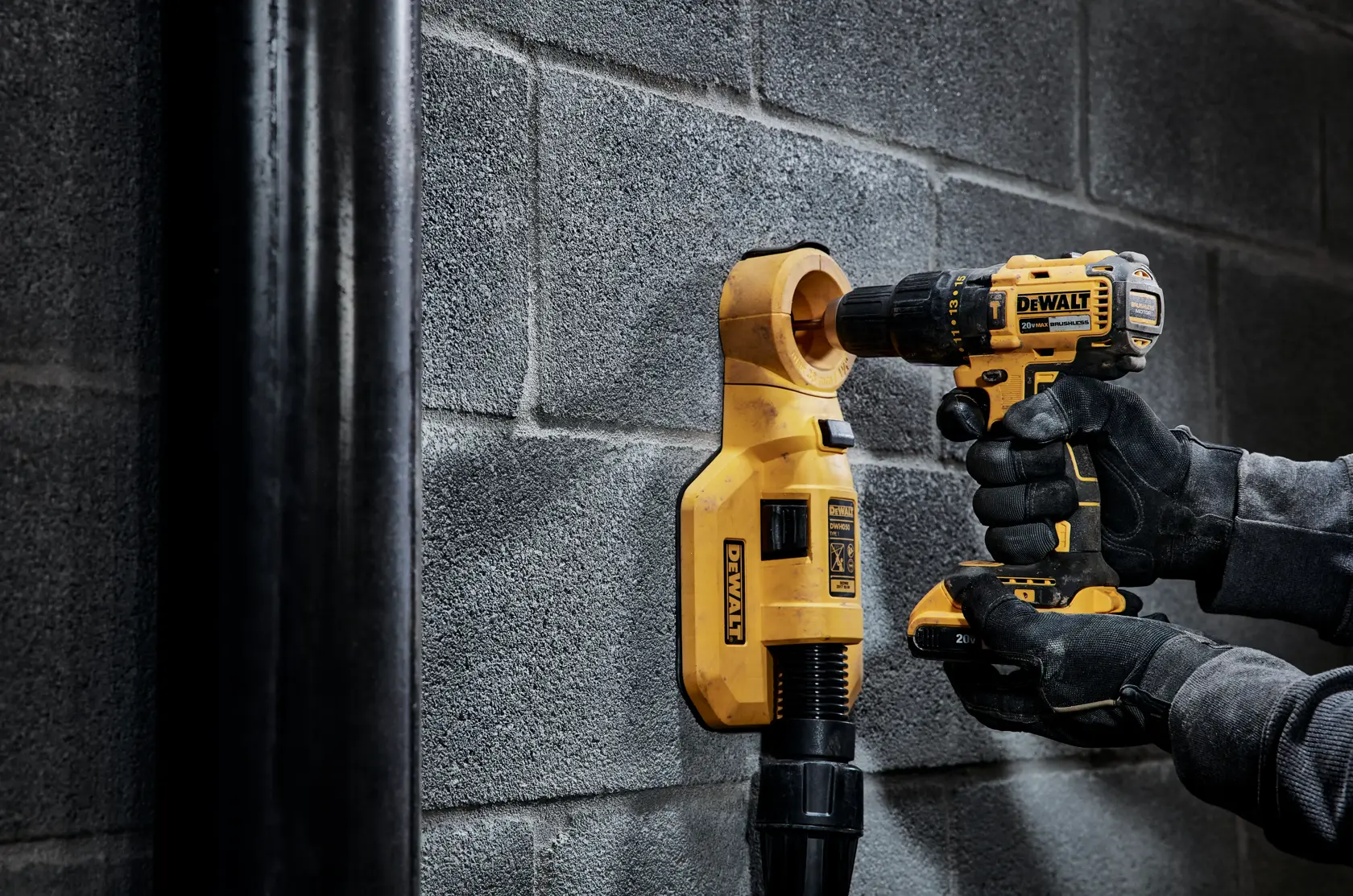 Una persona con guantes usa un taladro inalámbrico amarillo DEWALT para taladrar una pared de concreto, junto con un extractor de polvo DEWALT que recoge los residuos.