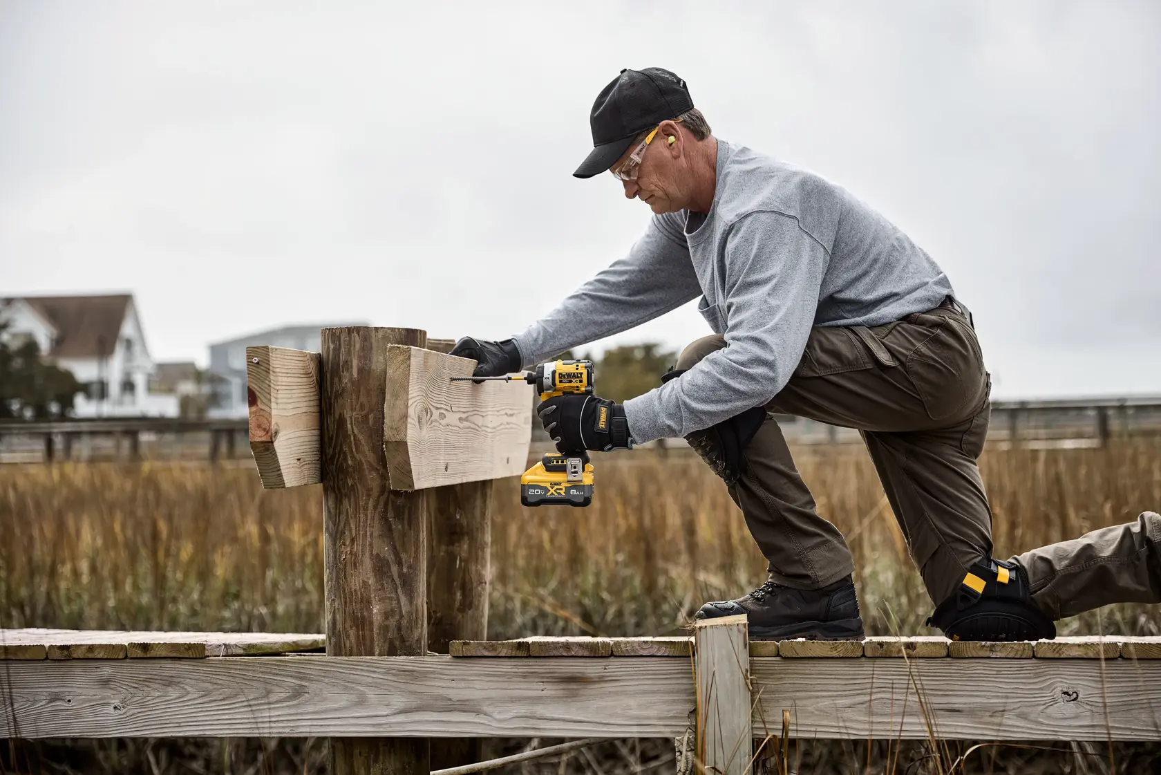 Persona usa taladro inalámbrico DEWALT para unir tablas de madera afuera, lleva guantes y ropa de trabajo.