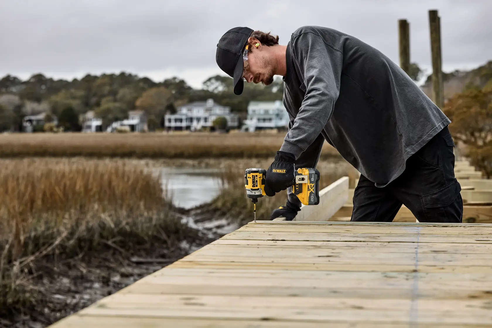 Persona usa taladro DEWALT para construir una pasarela de madera cerca del agua y casas.