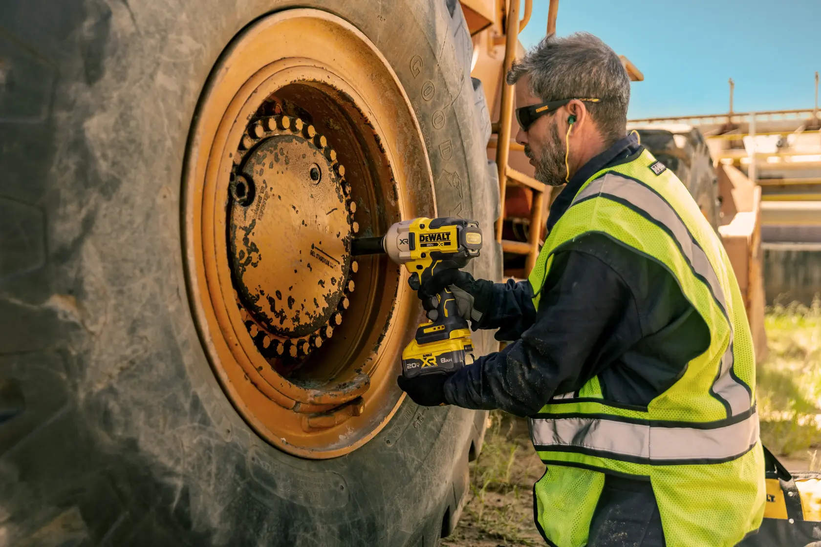 Persona usa llave de impacto DEWALT para ajustar pernos en la rueda de un vehículo industrial grande al aire libre.