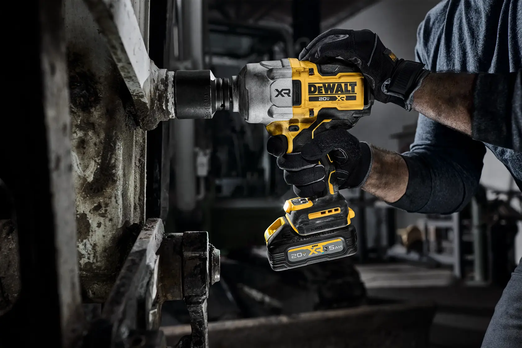 Manos con guantes usan una llave de impacto inalámbrica DEWALT en un perno metálico grande industrial.