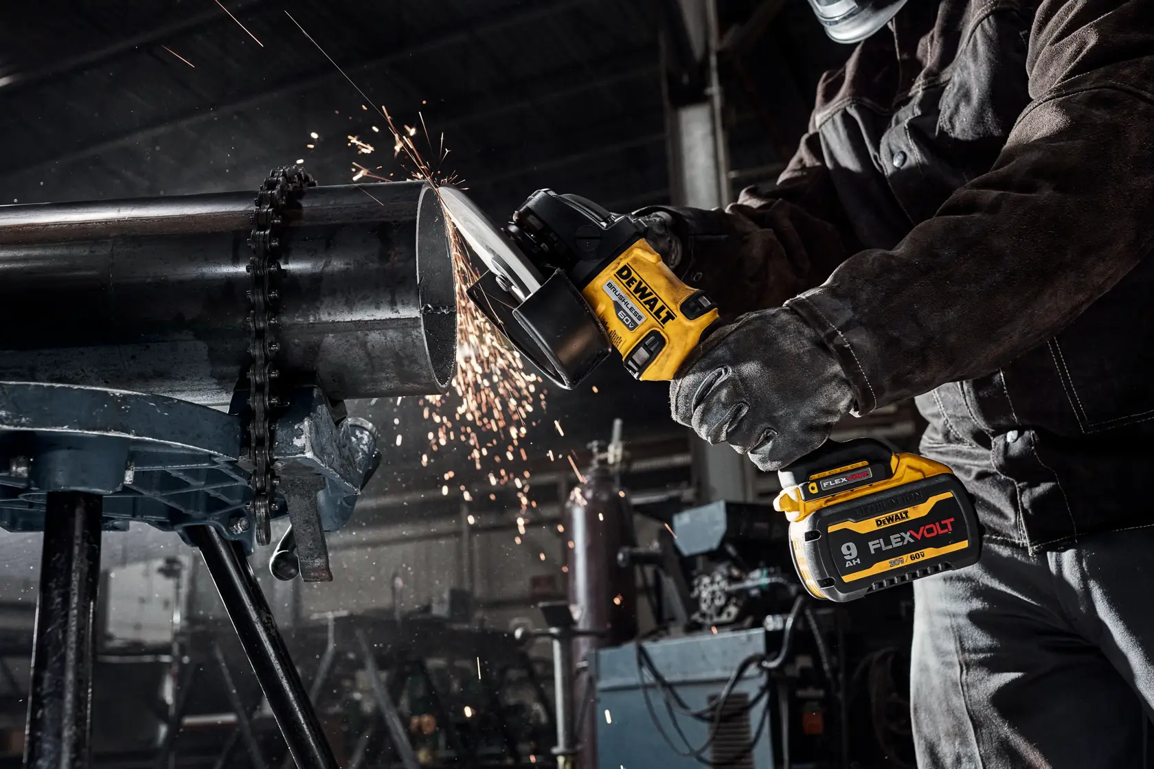 Una persona con equipo de protección utiliza una amoladora angular inalámbrica DEWALT para cortar un tubo de metal grande en un taller industrial, con chispas saltando durante el proceso de corte.