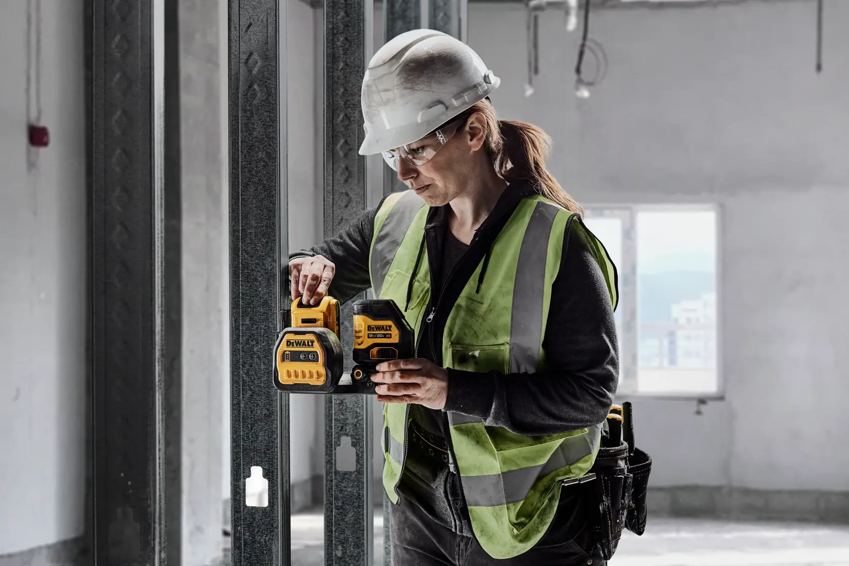 Una persona con casco de seguridad y chaleco reflectante está utilizando una herramienta DEWALT en un entorno de construcción sin terminar. El dispositivo DEWALT es amarillo y negro, y la persona parece estar ajustándolo o operándolo.