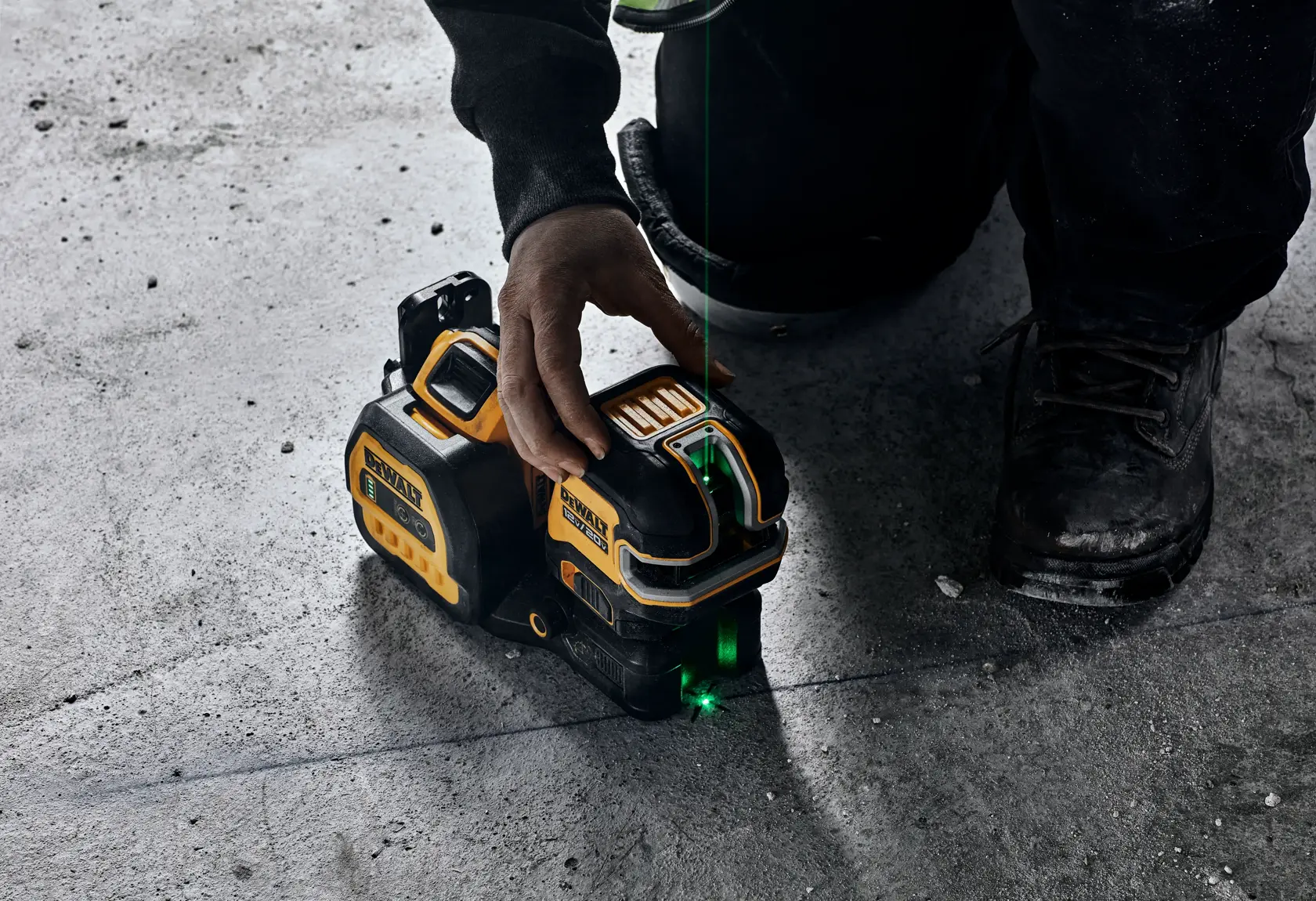 Una persona está utilizando un nivel láser verde DEWALT sobre un suelo de concreto, colocándolo para una medición precisa. El dispositivo emite una línea láser verde visible para alineación.