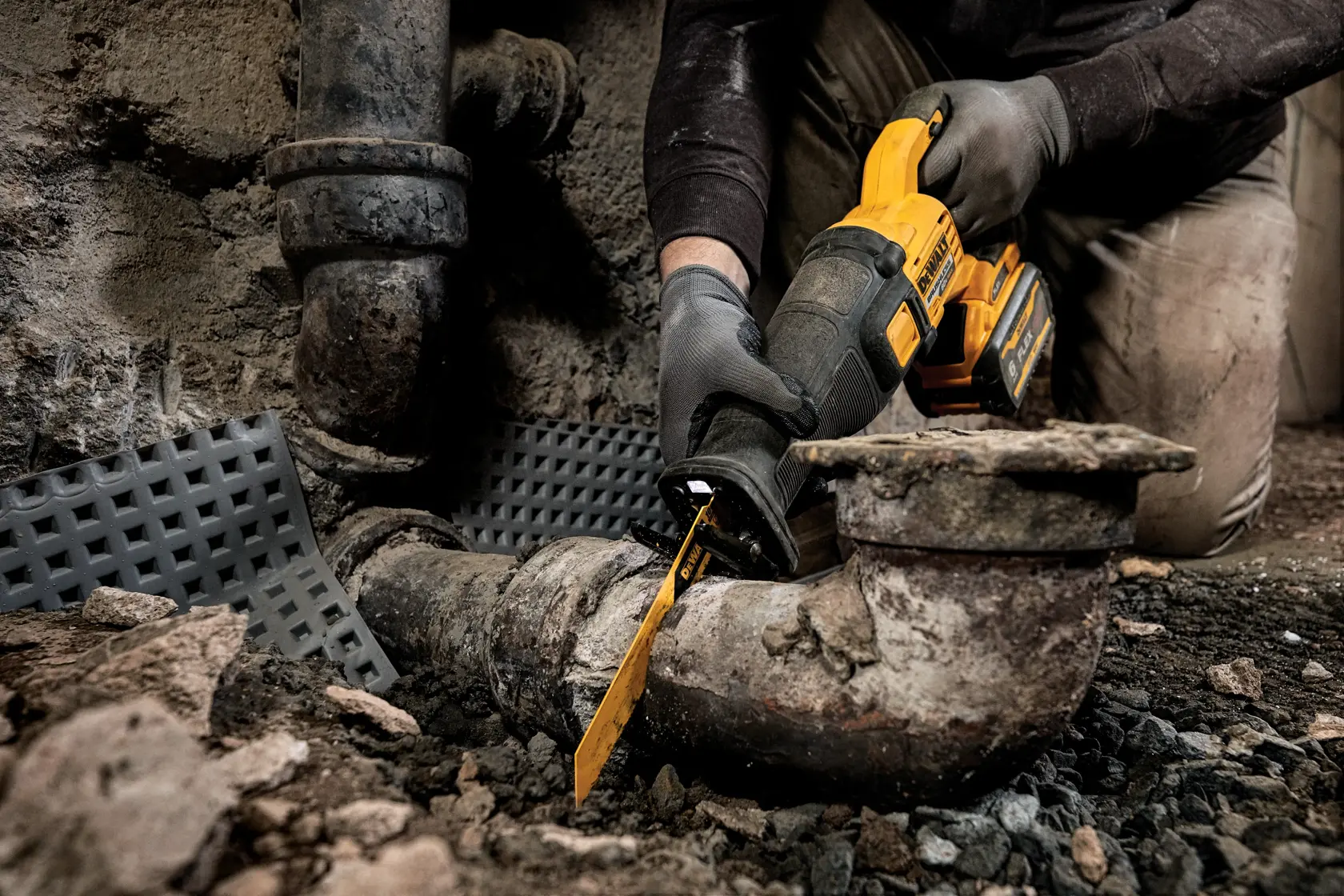 Una persona con guantes utiliza una sierra reciprocante DEWALT para cortar una tubería de metal antigua en un entorno industrial duro.