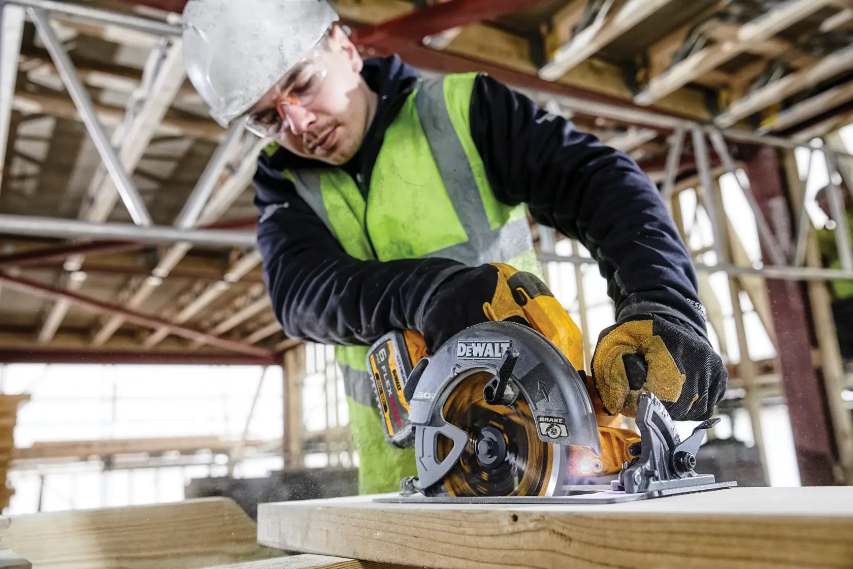 Trabajador corta madera con una sierra circular DEWALT DCS578T2 en obra, usando guantes y equipo de seguridad.