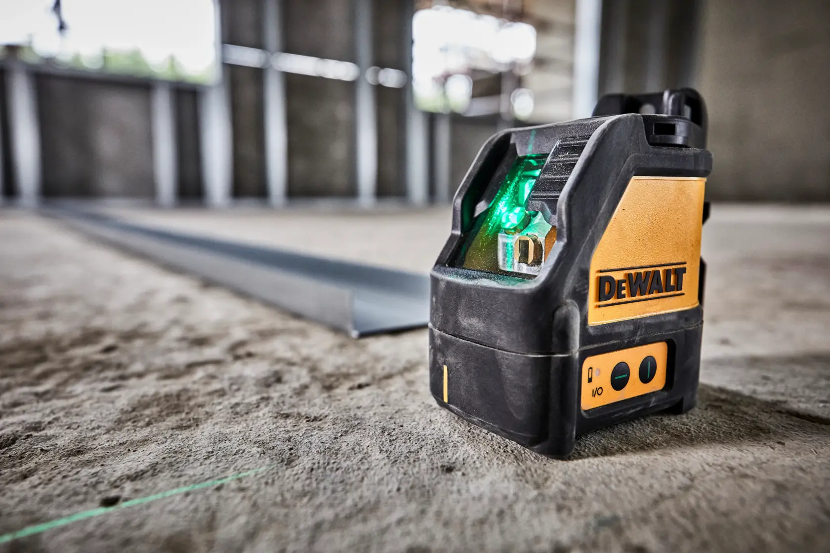Nivel láser de haz verde DEWALT DW088CG sobre suelo de cemento en obra.