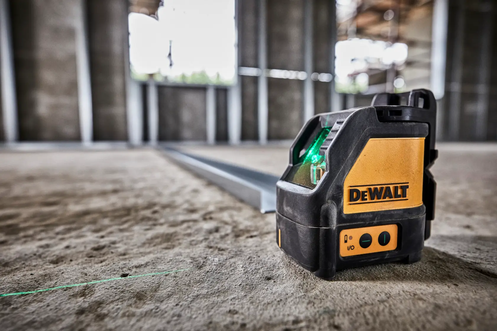 Nivel láser verde DEWALT DW088CG sobre suelo de concreto, proyectando línea verde recta.