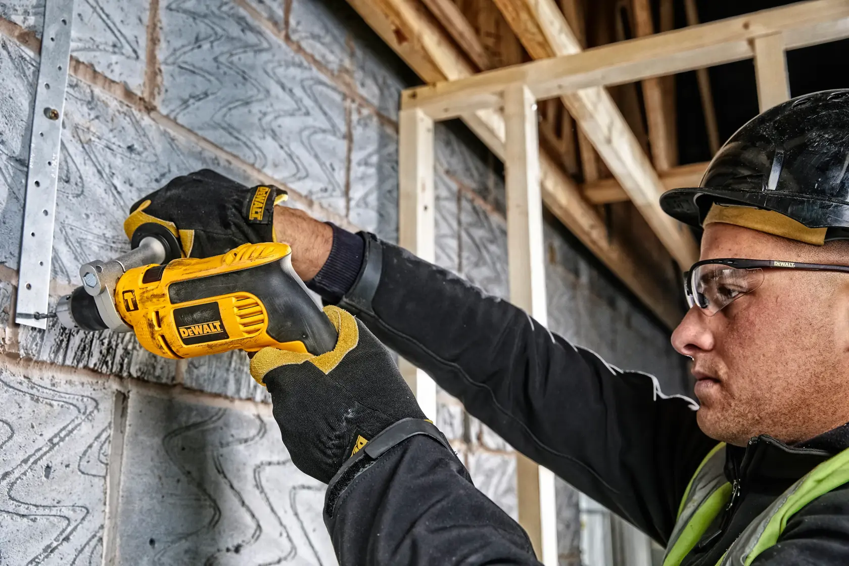 Trabajador con guantes usa taladro DEWALT DWD024K en muro. El rostro está difuminado por privacidad.