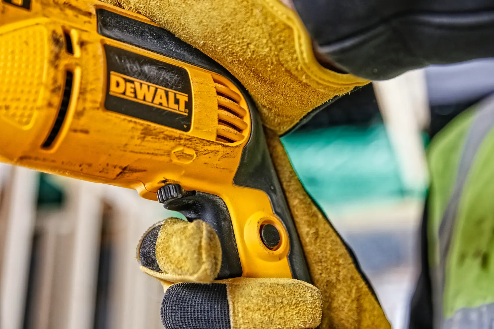 Primer plano de mano enguantada sosteniendo un taladro eléctrico DEWALT en una obra.