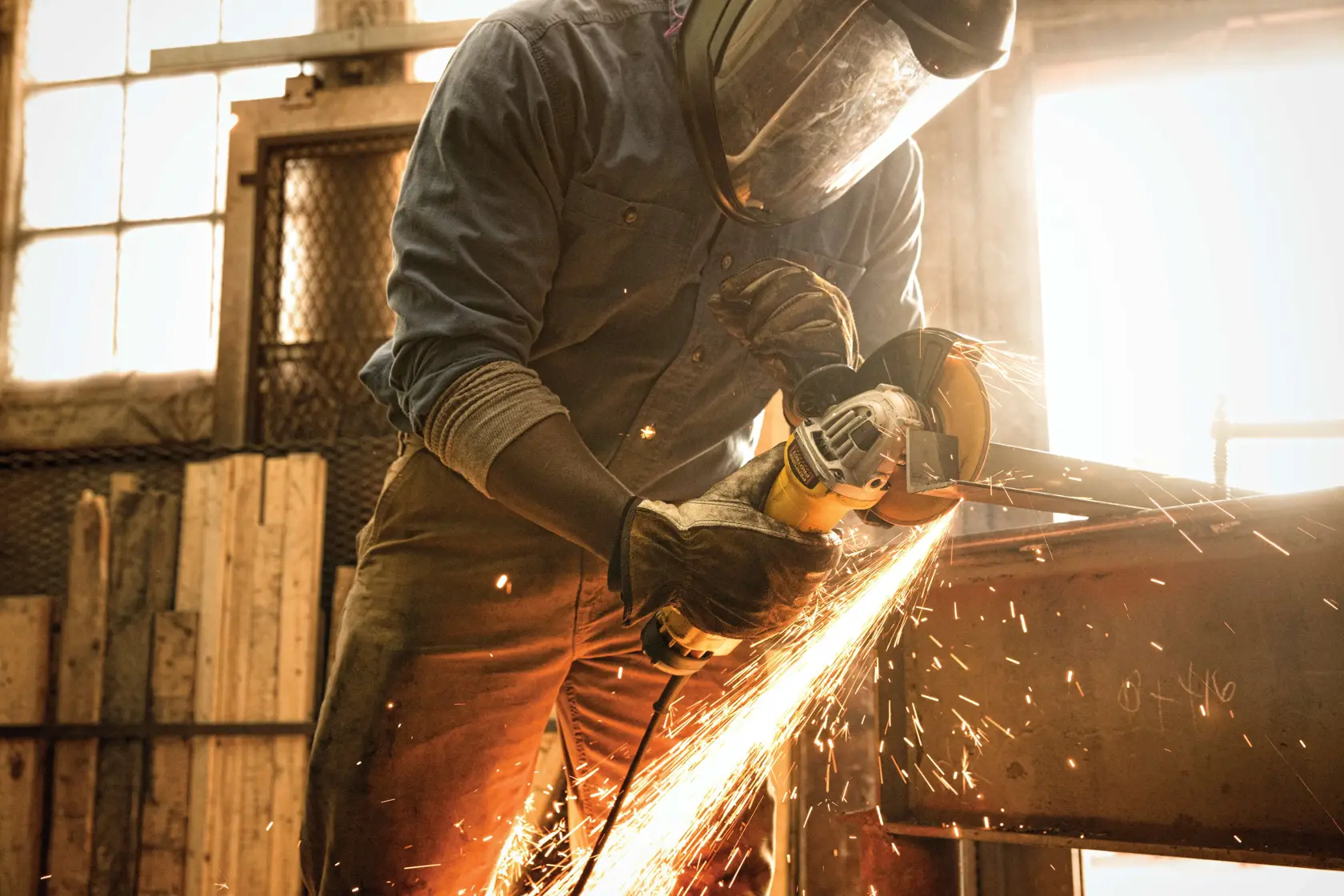 Una persona con equipo de protección utiliza una amoladora angular DEWALT DWE4314 para cortar una viga de metal, generando chispas brillantes en un taller.