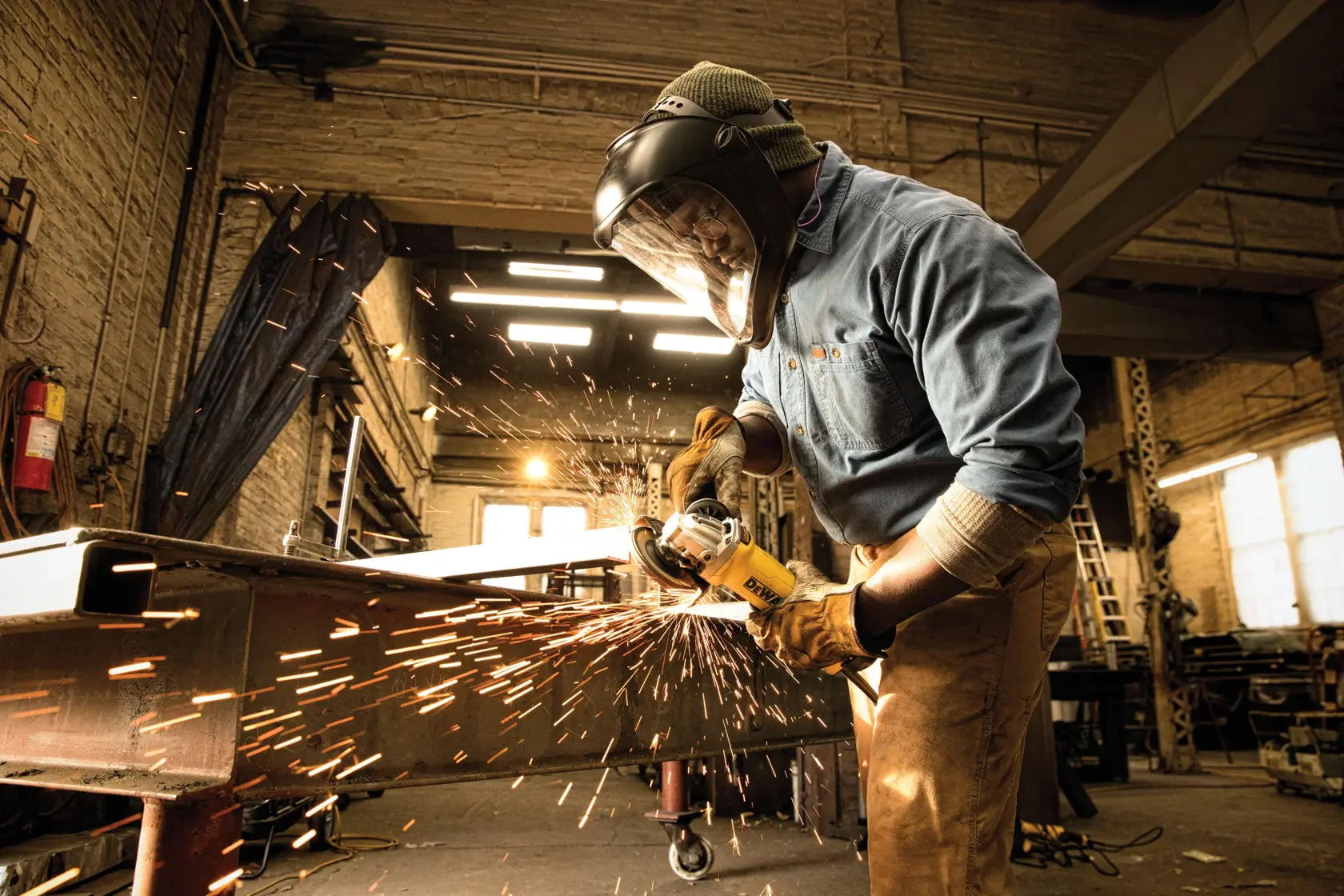 Un trabajador con guantes protectores y una pantalla facial utiliza una amoladora angular DEWALT para cortar o pulir metal, produciendo chispas en un taller industrial.