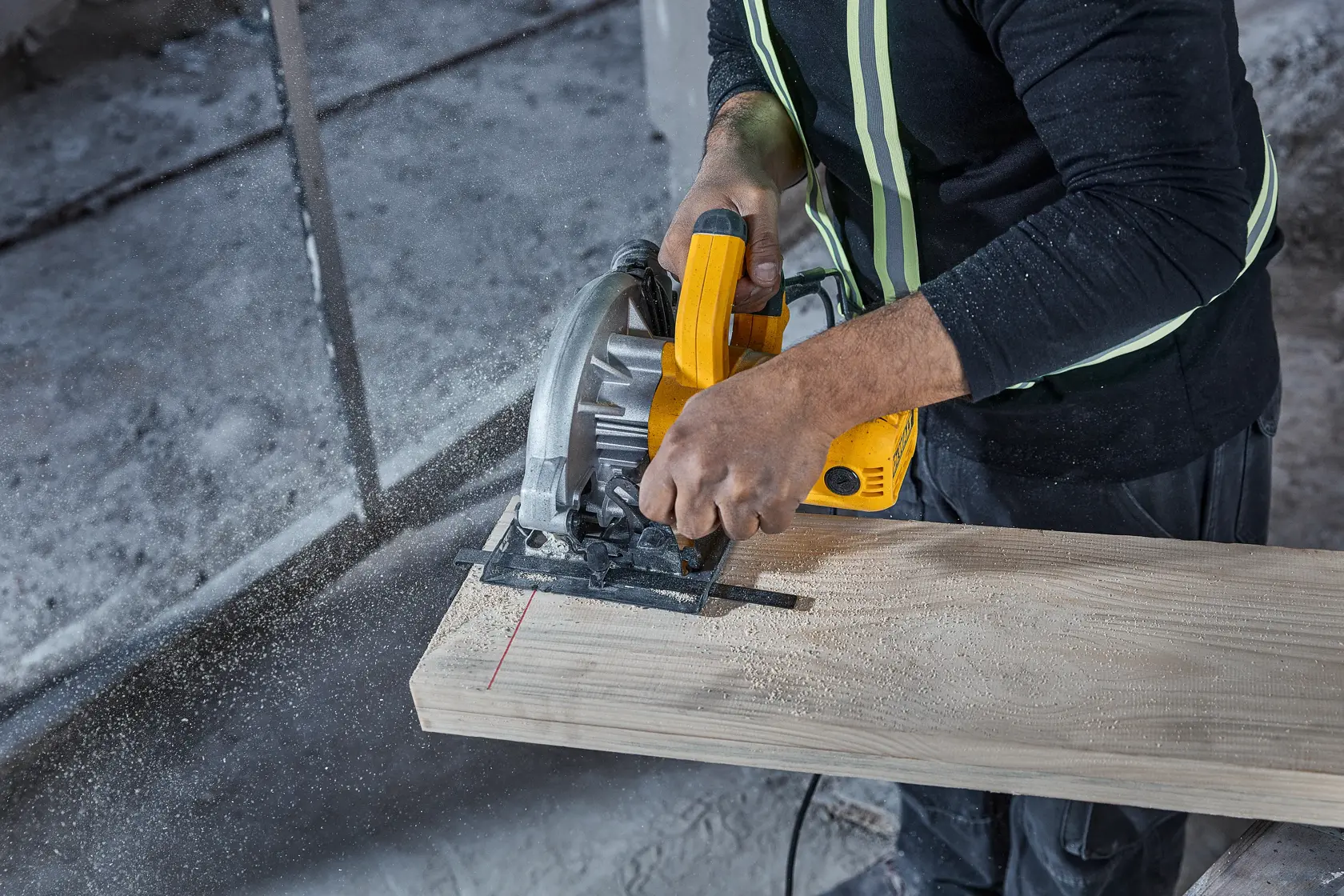 Una persona utiliza una sierra circular amarilla DEWALT (modelo DWE5615) para cortar una tabla de madera, con aserrín y equipo de seguridad visible.