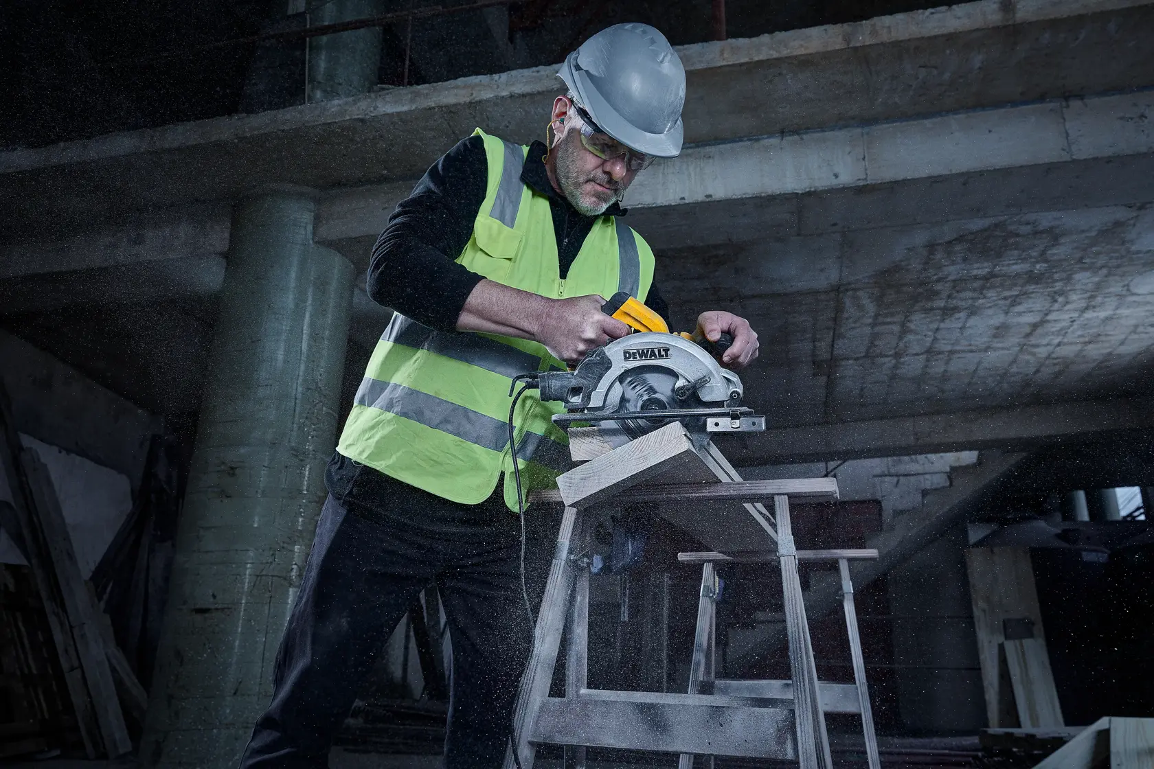 Una persona con casco de seguridad y chaleco reflectante utiliza una sierra circular DEWALT DWE5615 para cortar madera en una obra de construcción. El fondo muestra un edificio parcialmente construido y materiales de construcción dispersos.